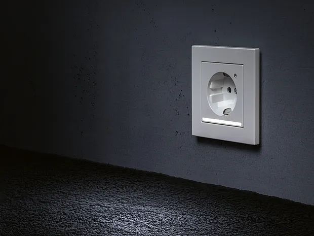 Beleuchtete Steckdose mit LED-Orientierungslicht an einer dunklen Wand